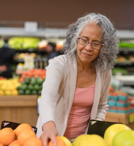 Older healthy woman reaching out for fruit at a grocery store.